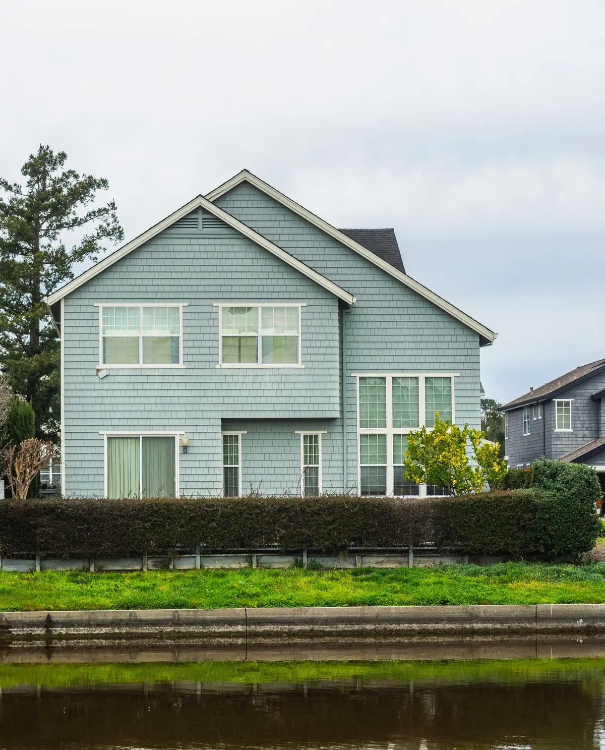 Two-story suburban house behind a trimmed hedge