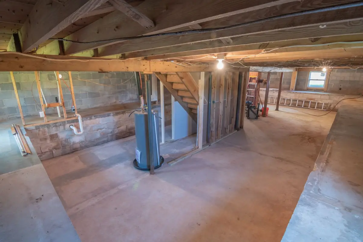 Unfinished basement with exposed beams, pipes and a water heater