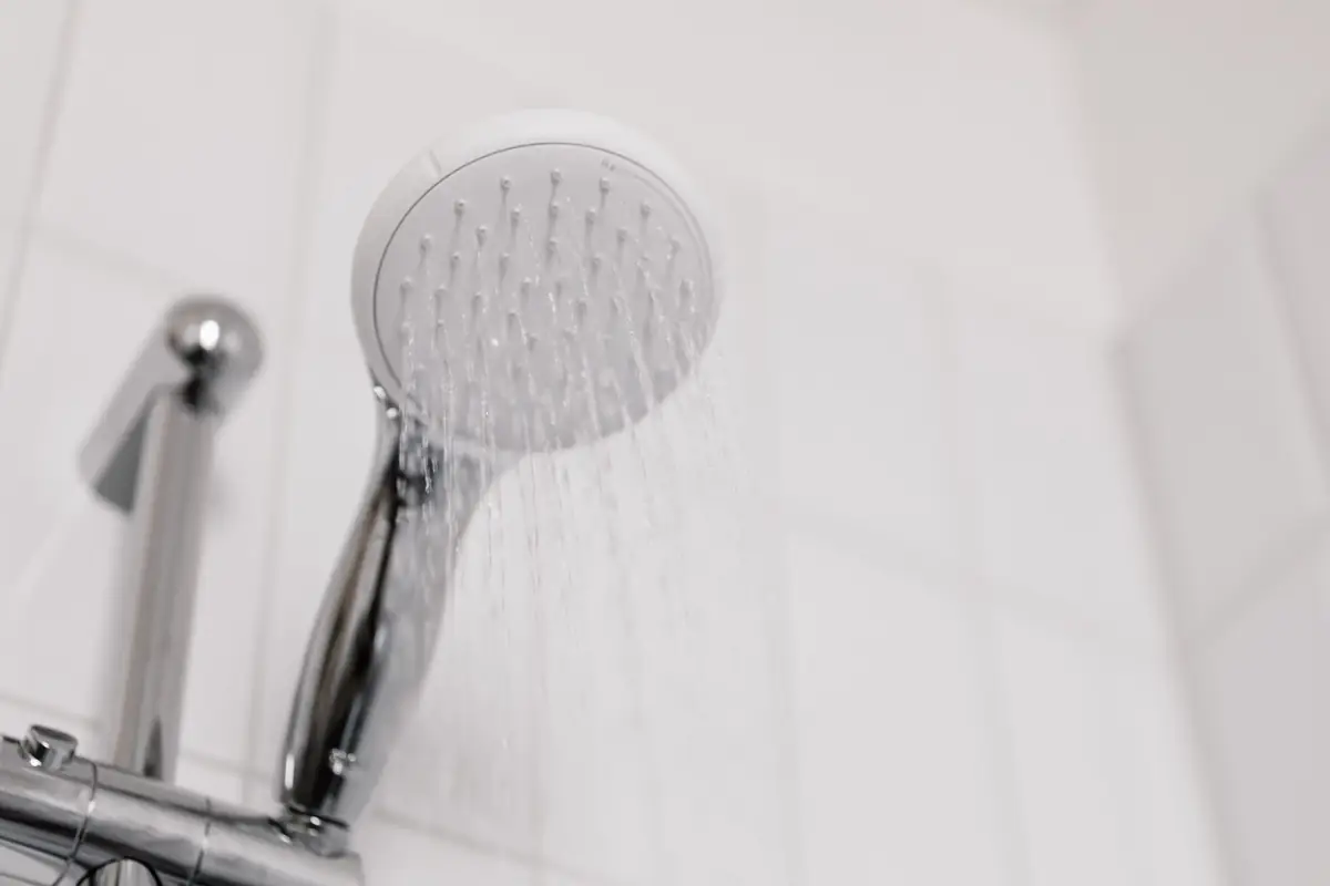 Chrome shower head with water running against white tile